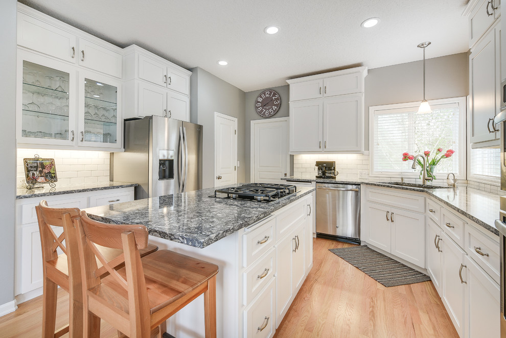 Mid-sized transitional l-shaped light wood floor and brown floor enclosed kitchen photo in Portland with a drop-in sink, shaker cabinets, white cabinets, quartz countertops, white backsplash, subway tile backsplash, an island and stainless steel appliances