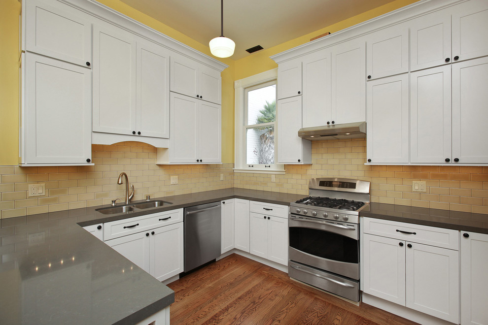 Design ideas for a traditional u-shaped kitchen pantry in San Francisco with an undermount sink, shaker cabinets, white cabinets, quartz benchtops, yellow splashback, glass tile splashback, stainless steel appliances and medium hardwood floors.
