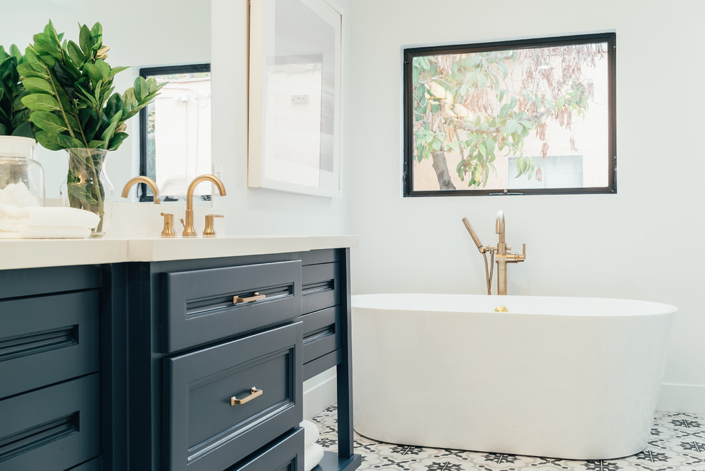 Photo of a mediterranean bathroom in Los Angeles with recessed-panel cabinets, blue cabinets, a freestanding tub, white walls, multi-coloured floor and white benchtops.