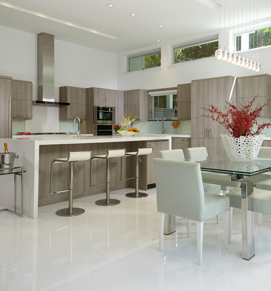 Photo of a large contemporary galley open plan kitchen in Miami with a drop-in sink, flat-panel cabinets, grey cabinets, quartz benchtops, green splashback, glass sheet splashback, stainless steel appliances, marble floors and with island.