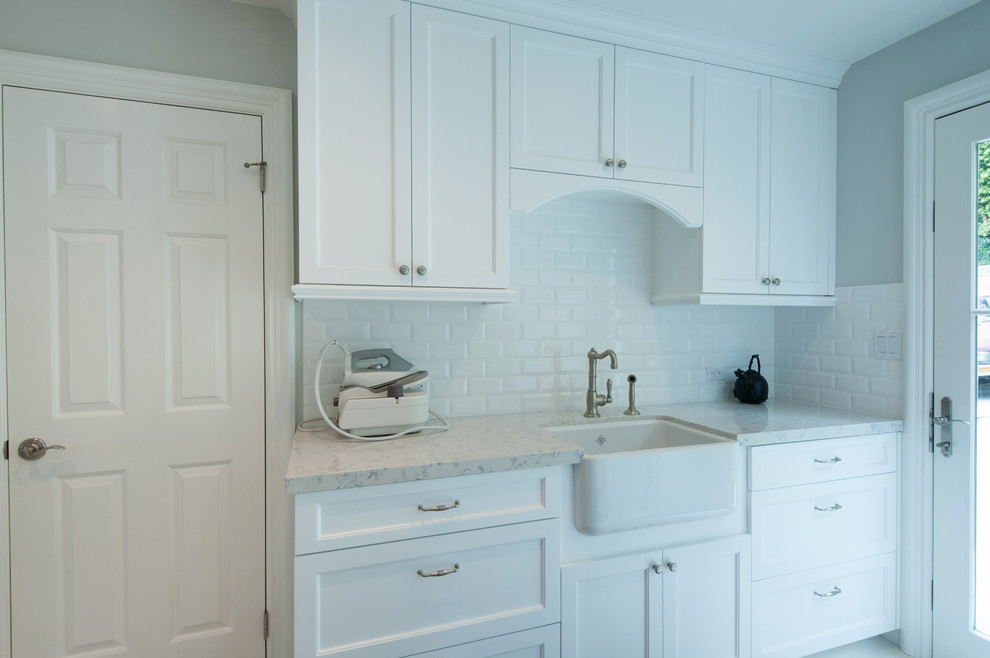 Design ideas for a mid-sized traditional galley dedicated laundry room in Los Angeles with a farmhouse sink, shaker cabinets, white cabinets, quartz benchtops, grey walls, porcelain floors and a side-by-side washer and dryer.
