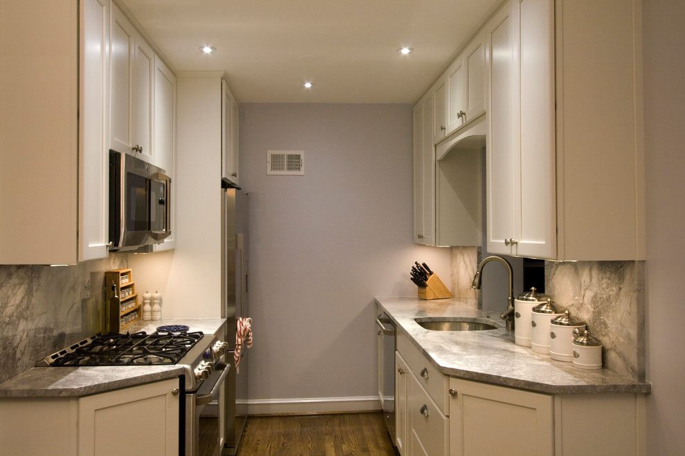 Enclosed kitchen - small transitional galley medium tone wood floor enclosed kitchen idea in DC Metro with an undermount sink, recessed-panel cabinets, white cabinets, quartz countertops, gray backsplash, stone slab backsplash, stainless steel appliances and no island
