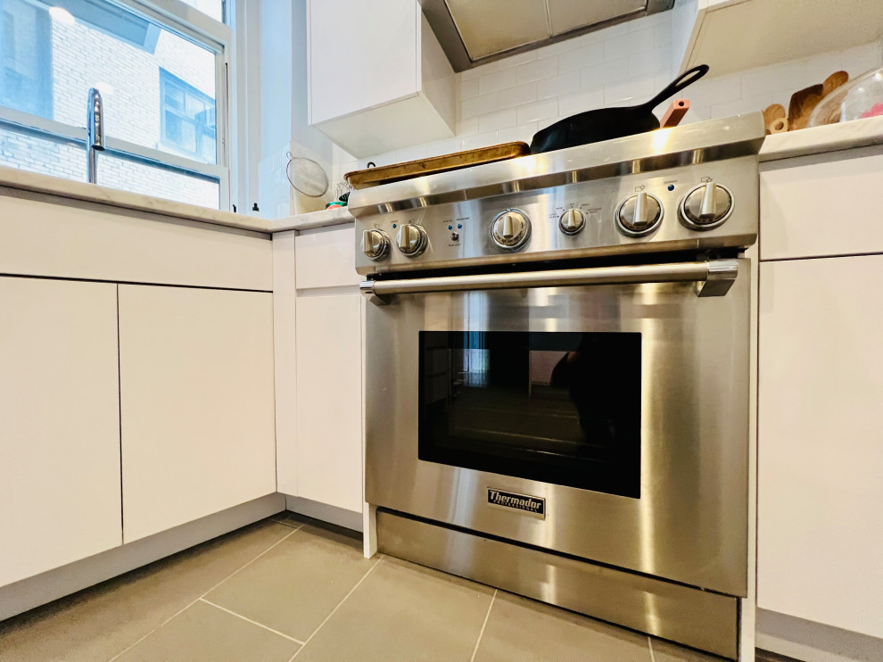 ニューヨークにある高級な広い北欧スタイルのおしゃれなキッチン (ドロップインシンク、フラットパネル扉のキャビネット、白いキャビネット、大理石カウンター、白いキッチンパネル、サブウェイタイルのキッチンパネル、シルバーの調理設備、スレートの床、グレーの床、マルチカラーのキッチンカウンター) の写真