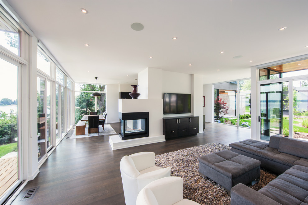 Photo of a contemporary living room in Ottawa with white walls, dark hardwood floors, a two-sided fireplace and a wall-mounted tv.
