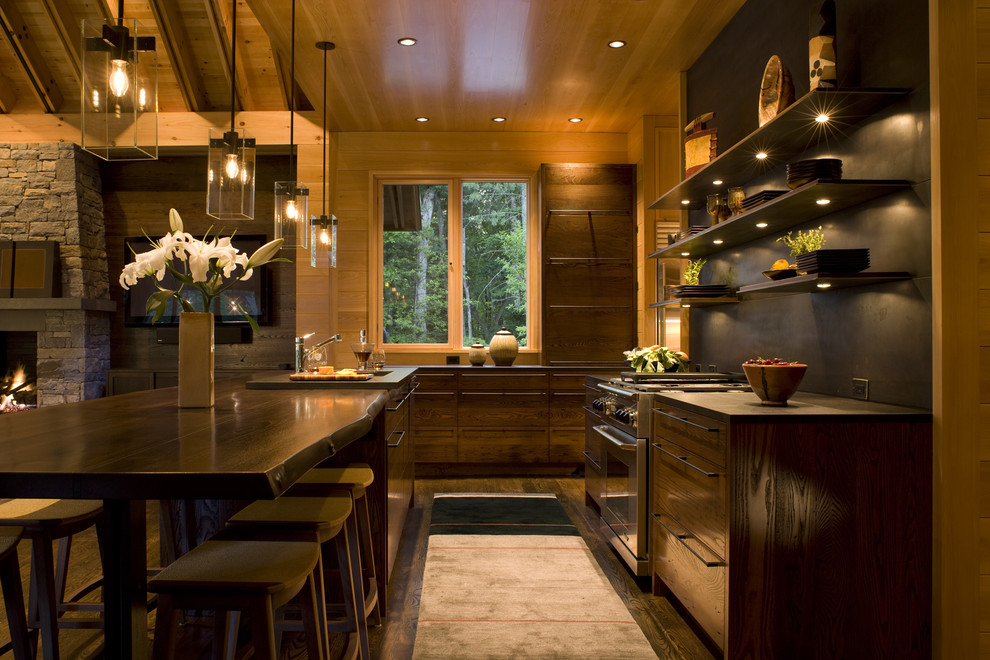 This is an example of a transitional galley open plan kitchen in Charlotte with flat-panel cabinets, with island, a drop-in sink, wood benchtops, black splashback, metal splashback, stainless steel appliances, dark hardwood floors and brown floor.
