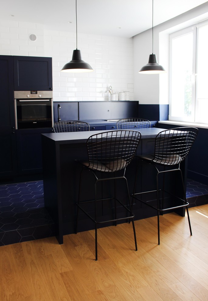 Design ideas for a mid-sized industrial galley open plan kitchen in London with a single-bowl sink, beaded inset cabinets, blue cabinets, laminate benchtops, blue splashback, brick splashback, black appliances, porcelain floors, with island, blue floor and blue benchtop.