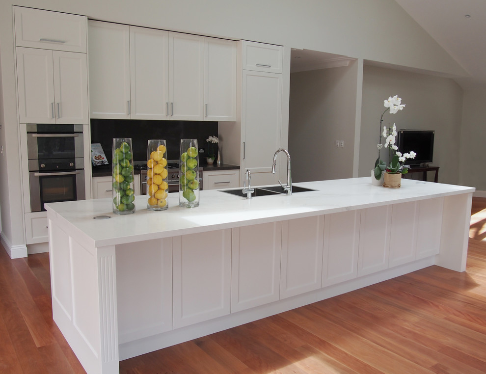 This is an example of a large transitional galley eat-in kitchen in Sydney with a drop-in sink, shaker cabinets, white cabinets, quartz benchtops, metallic splashback, stone slab splashback, stainless steel appliances, medium hardwood floors and multiple islands.
