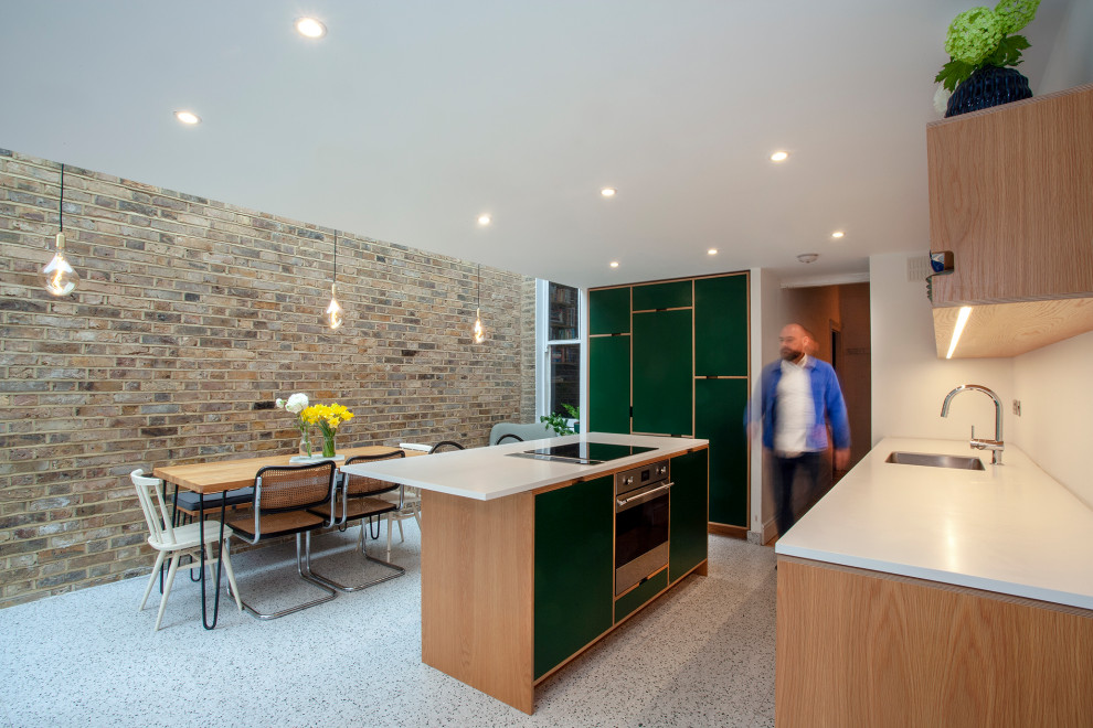 Design ideas for a large contemporary galley eat-in kitchen in London with a single-bowl sink, flat-panel cabinets, green cabinets, solid surface benchtops, white splashback, black appliances, terrazzo floors, with island, grey floor and white benchtop.