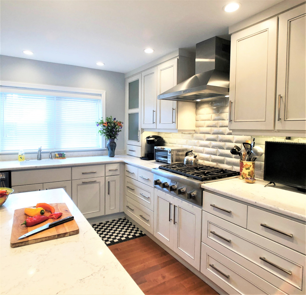 Mid-sized eclectic l-shaped kitchen in Philadelphia with an undermount sink, recessed-panel cabinets, white cabinets, quartzite benchtops, white splashback, stainless steel appliances, medium hardwood floors, with island and white benchtop.