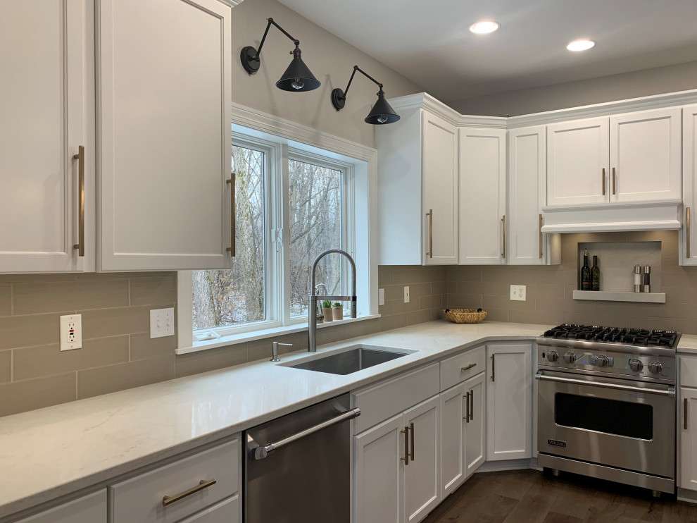 Kitchen - large transitional l-shaped medium tone wood floor kitchen idea in Milwaukee with recessed-panel cabinets, white cabinets, quartz countertops, beige backsplash, stainless steel appliances, an island and white countertops