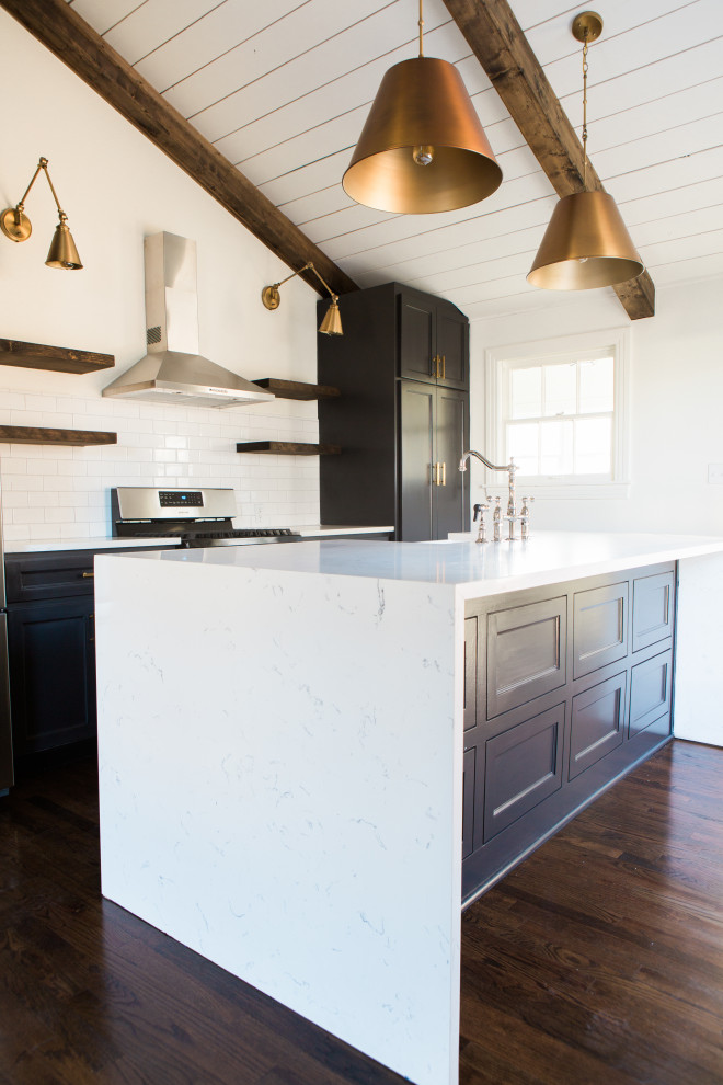 Large country single-wall kitchen in Dallas with a farmhouse sink, black cabinets, granite benchtops, white splashback, ceramic splashback, stainless steel appliances, dark hardwood floors, with island, brown floor and exposed beam.