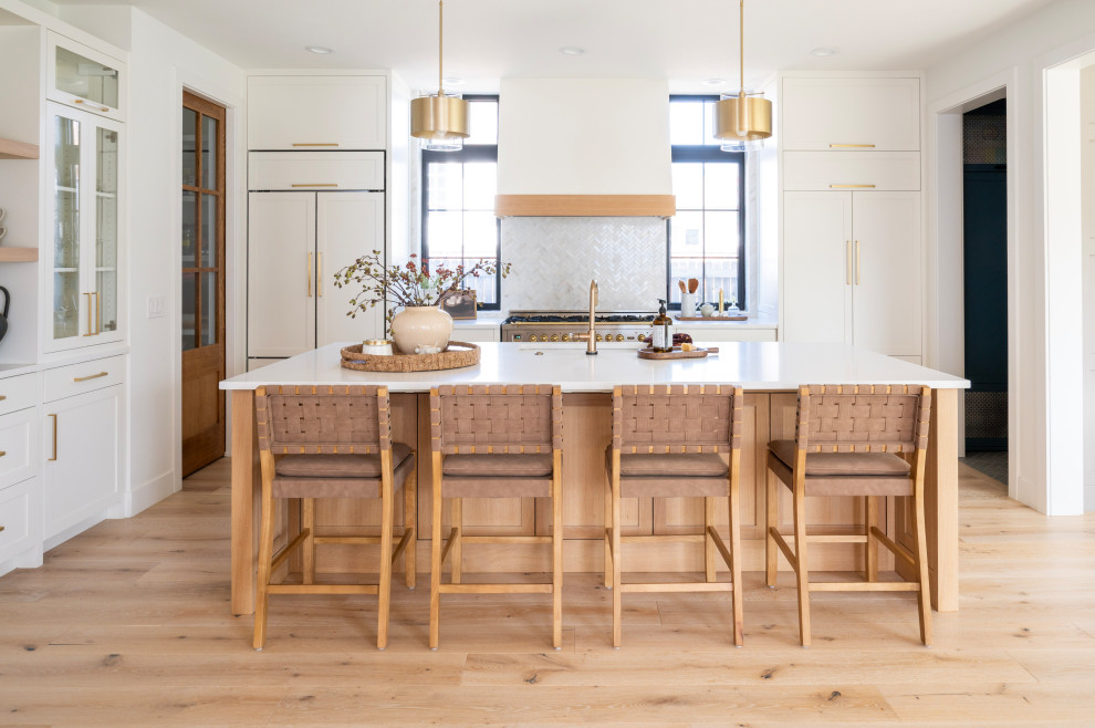Transitional l-shaped light wood floor and beige floor kitchen photo in Denver with an undermount sink, shaker cabinets, white cabinets, white backsplash, mosaic tile backsplash, stainless steel appliances, an island and white countertops