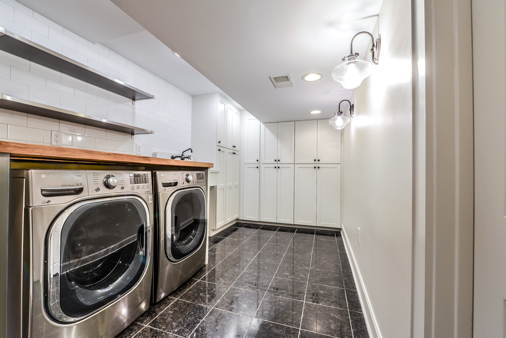 Inspiration for a mid-sized contemporary utility room in Cincinnati with an utility sink, shaker cabinets, white cabinets, wood benchtops, white walls, marble floors, a side-by-side washer and dryer, black floor and brown benchtop.