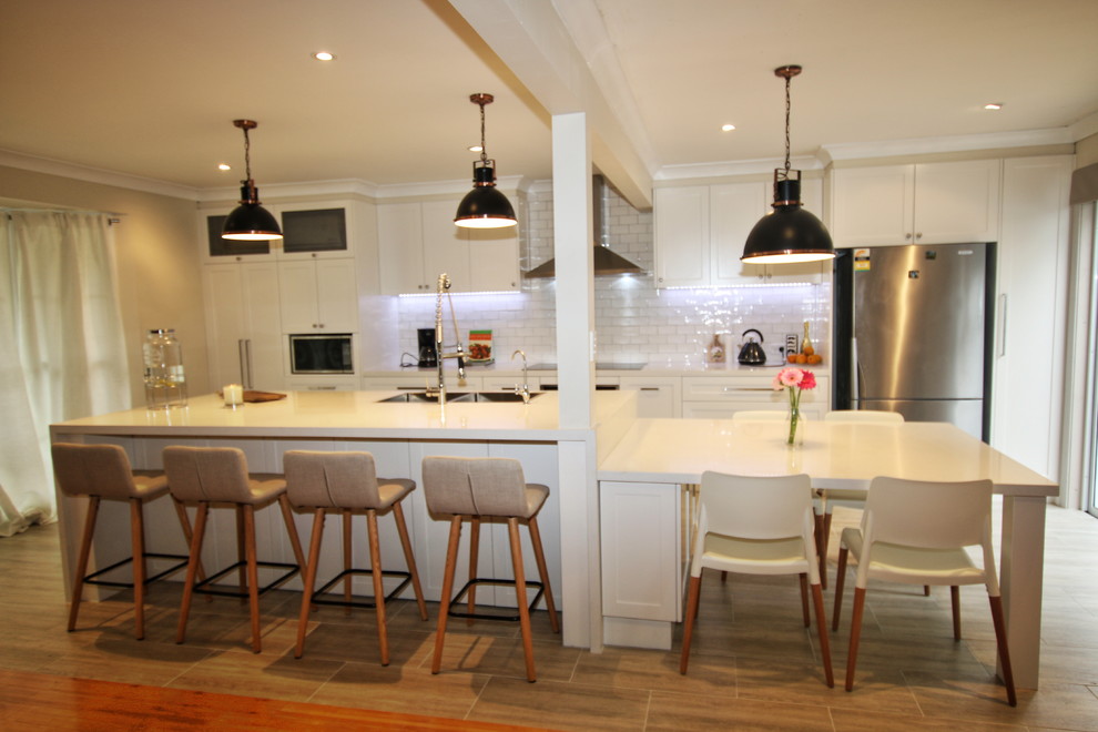 Photo of a large transitional single-wall kitchen in Sydney with a double-bowl sink, shaker cabinets, white cabinets, quartz benchtops, white splashback, subway tile splashback, stainless steel appliances, porcelain floors and with island.