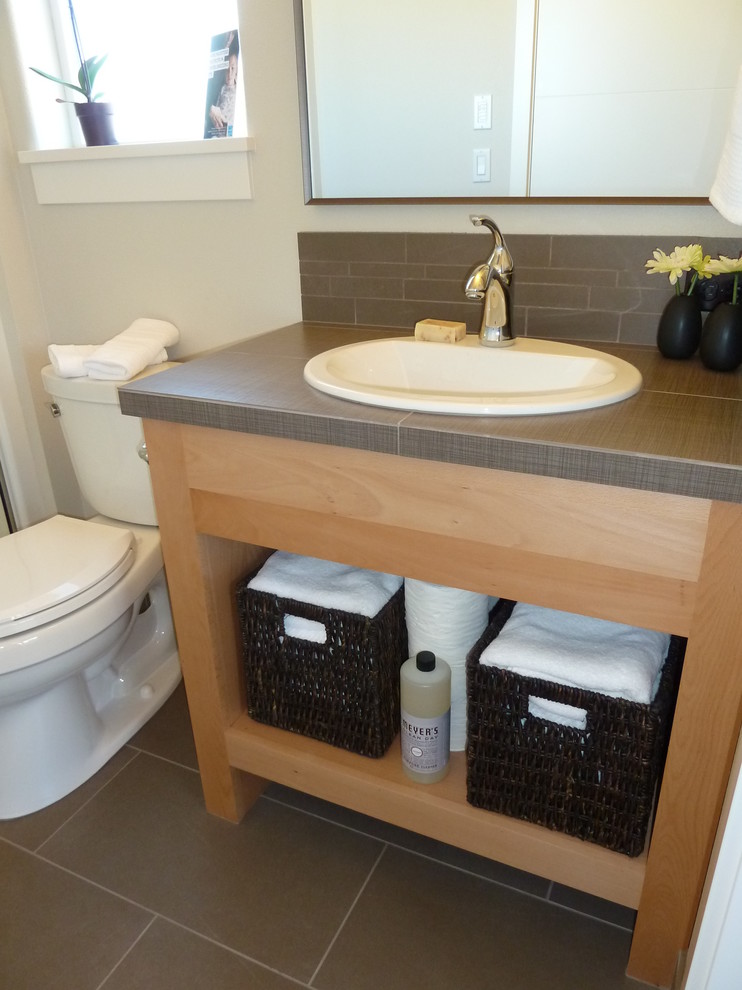 Exemple d'un petit WC et toilettes tendance en bois clair avec un carrelage gris, un mur blanc et un plan de toilette en carrelage.