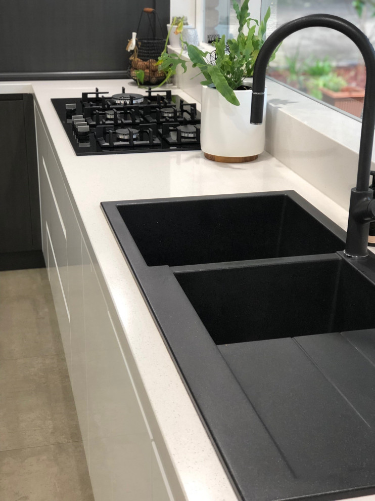 This is an example of a large contemporary l-shaped kitchen pantry in Melbourne with a double-bowl sink, white cabinets, quartz benchtops, black appliances, terra-cotta floors and with island.