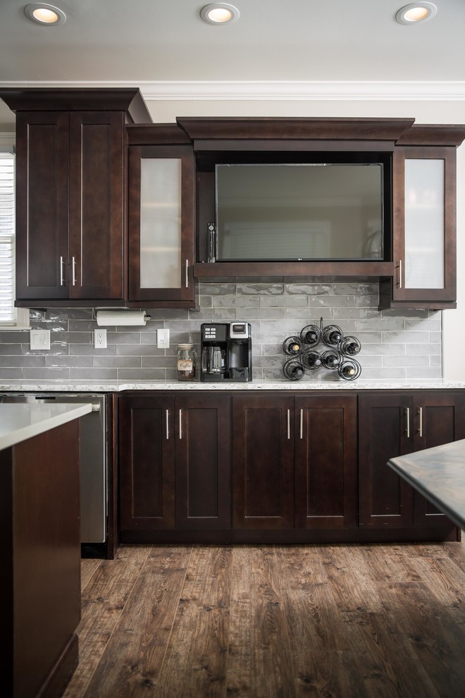 Inspiration for a mid-sized transitional l-shaped eat-in kitchen in Atlanta with an undermount sink, recessed-panel cabinets, dark wood cabinets, quartzite benchtops, grey splashback, ceramic splashback, stainless steel appliances, laminate floors, with island, brown floor and white benchtop.