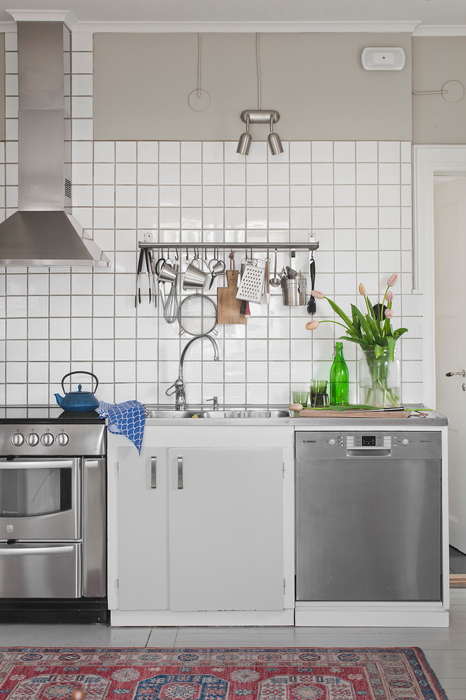 Design ideas for a small scandinavian single-wall kitchen in Stockholm with a double-bowl sink, flat-panel cabinets, grey cabinets, stainless steel benchtops, white splashback, porcelain splashback, stainless steel appliances and painted wood floors.