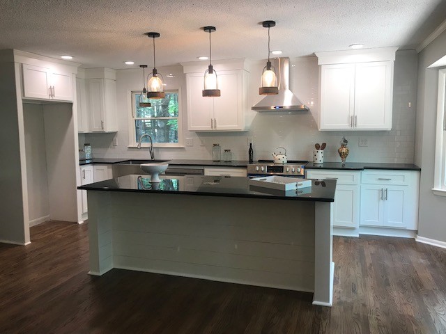 Inspiration for a mid-sized transitional l-shaped medium tone wood floor and brown floor eat-in kitchen remodel with a farmhouse sink, shaker cabinets, white cabinets, granite countertops, white backsplash, subway tile backsplash, stainless steel appliances, an island and black countertops
