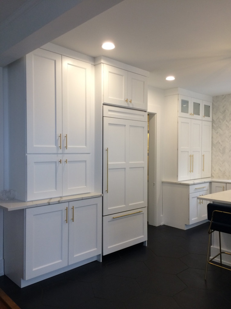 Photo of a mid-sized transitional l-shaped eat-in kitchen in New York with shaker cabinets, white cabinets, quartzite benchtops, grey splashback, stone tile splashback, ceramic floors, with island, black floor, white benchtop and a farmhouse sink.