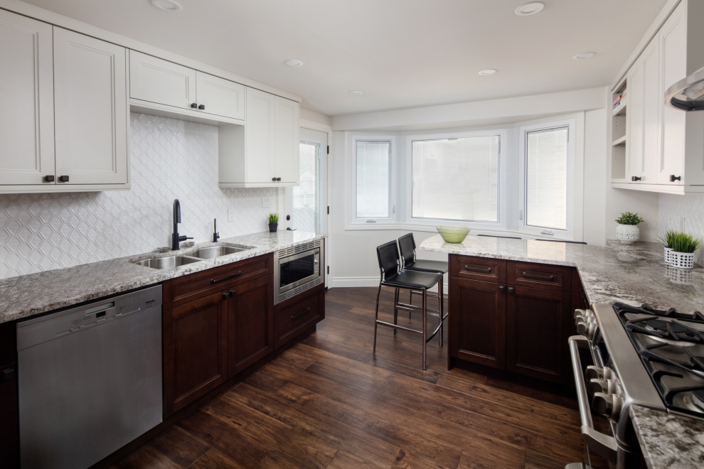 This is an example of a mid-sized transitional l-shaped kitchen in Toronto with an undermount sink, shaker cabinets, dark wood cabinets, granite benchtops, white splashback, porcelain splashback, stainless steel appliances, medium hardwood floors, a peninsula, brown floor and grey benchtop.