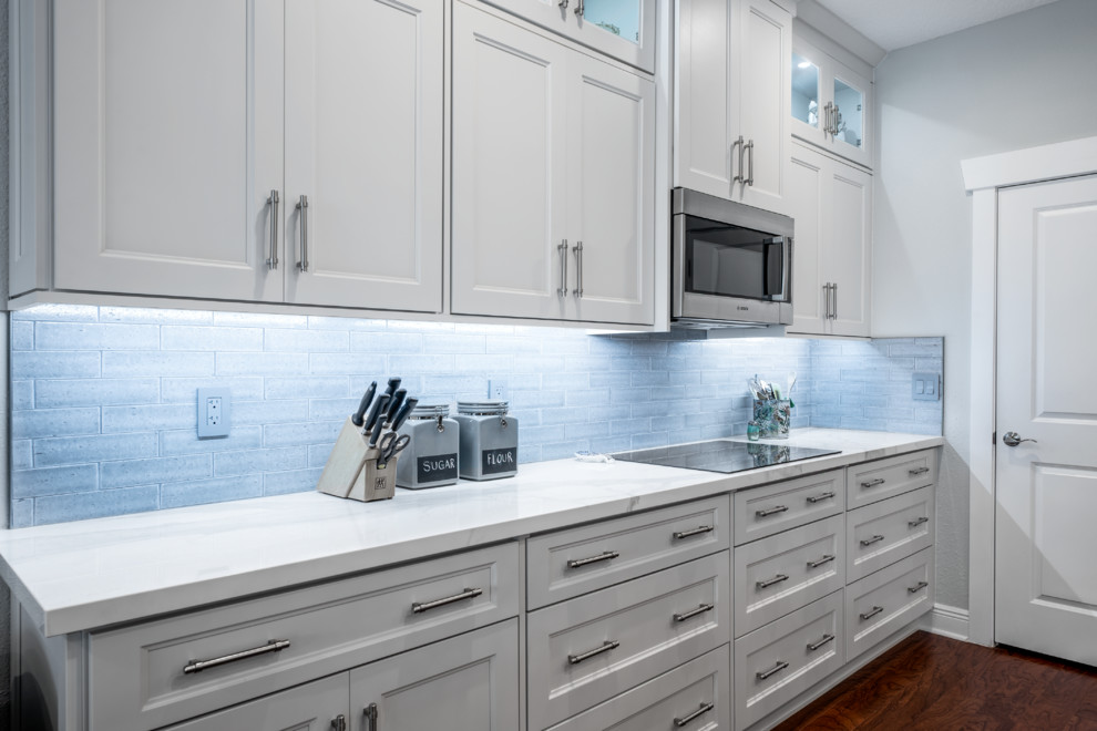 Mid-sized transitional l-shaped eat-in kitchen in Tampa with an undermount sink, shaker cabinets, white cabinets, tile benchtops, grey splashback, subway tile splashback, black appliances, medium hardwood floors, with island, brown floor and white benchtop.