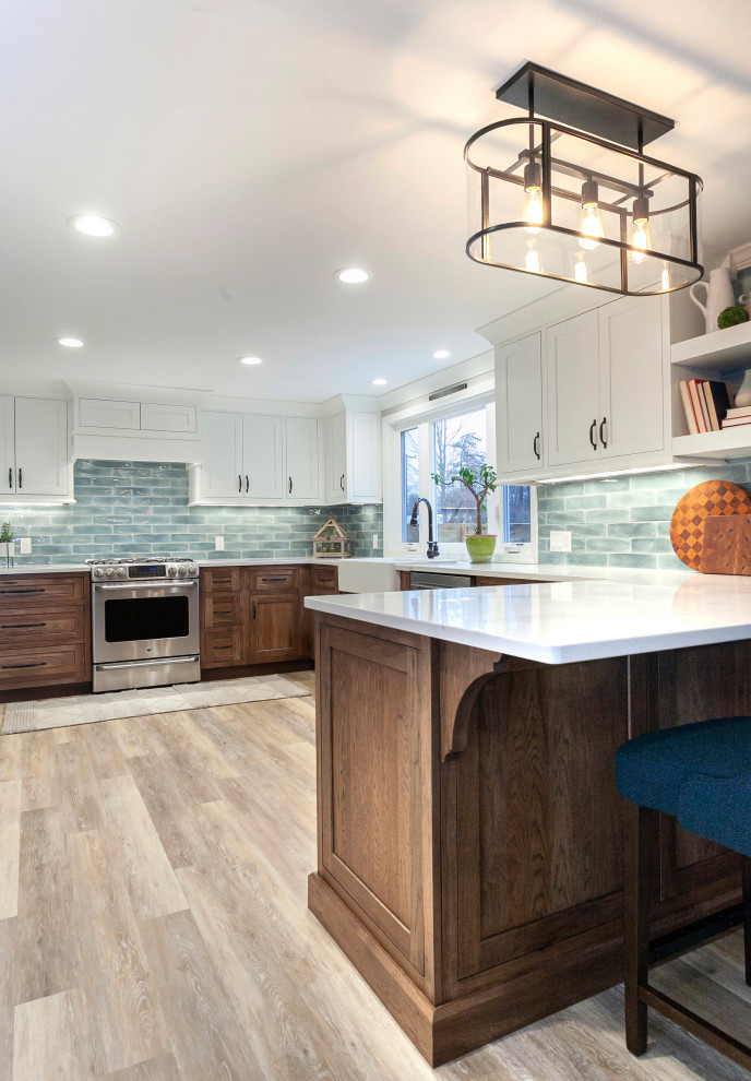 This is an example of a large transitional u-shaped eat-in kitchen in Bridgeport with a farmhouse sink, recessed-panel cabinets, brown cabinets, quartz benchtops, blue splashback, subway tile splashback, stainless steel appliances, light hardwood floors, no island, beige floor and white benchtop.