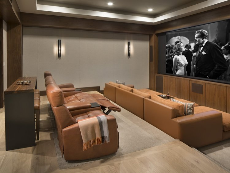 Aménagement d'une salle de cinéma contemporaine de taille moyenne et fermée avec un mur gris, un sol en bois brun et un téléviseur fixé au mur.