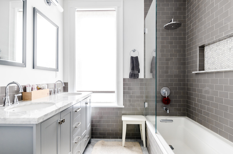 Photo of a transitional bathroom in New York with shaker cabinets, grey cabinets, a drop-in tub, gray tile, subway tile, white walls and an undermount sink.