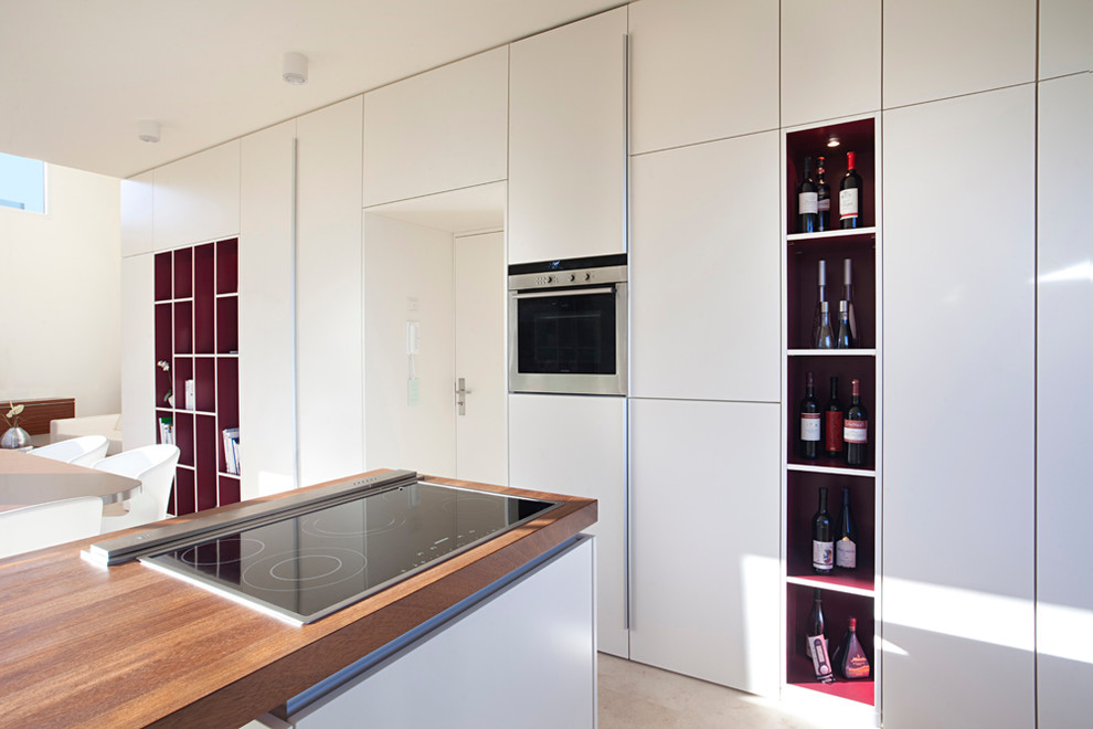 Photo of a contemporary open plan kitchen in Leipzig with flat-panel cabinets, white cabinets, wood benchtops, panelled appliances, limestone floors and with island.