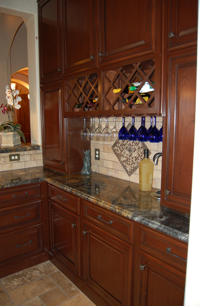 This is an example of a mid-sized traditional u-shaped seated home bar in Phoenix with raised-panel cabinets, dark wood cabinets, granite benchtops, beige splashback, stone tile splashback, travertine floors and an undermount sink.