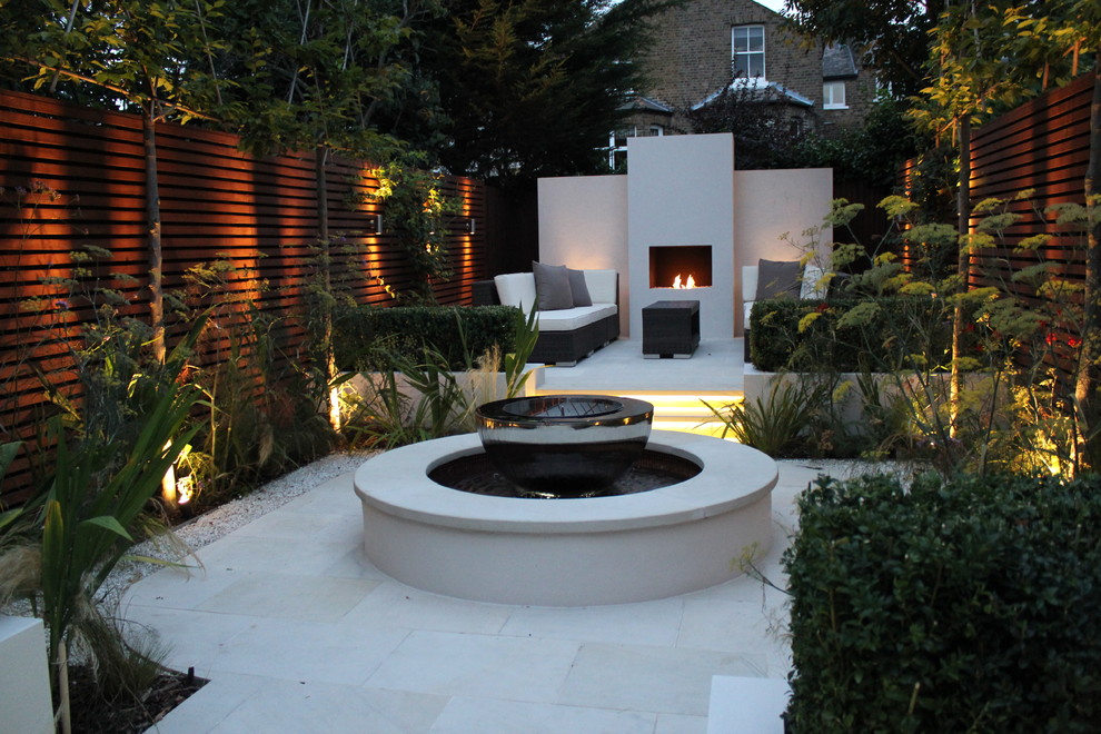 Photo of a mid-sized contemporary courtyard partial sun formal garden for spring in London with a fire feature and natural stone pavers.