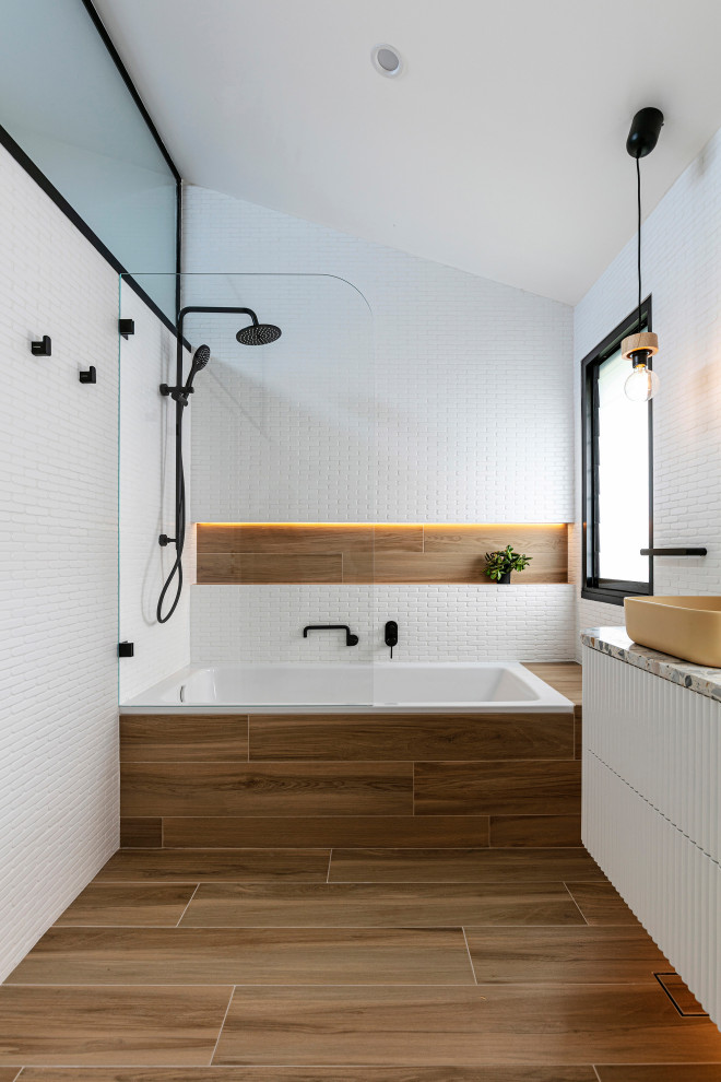 This is an example of a mid-sized beach style kids bathroom in Sydney with white cabinets, a drop-in tub, a shower/bathtub combo, a two-piece toilet, white tile, ceramic tile, white walls, ceramic floors, a vessel sink, terrazzo benchtops, brown floor, an open shower, multi-coloured benchtops, a shower seat, a double vanity, a floating vanity and vaulted.