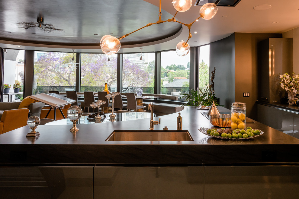 Photo of an expansive contemporary u-shaped eat-in kitchen in Los Angeles with an undermount sink, flat-panel cabinets, grey cabinets, granite benchtops, black splashback, stone slab splashback, stainless steel appliances, multiple islands, black benchtop, porcelain floors and yellow floor.