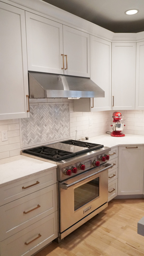 Transitional light wood floor open concept kitchen photo with a farmhouse sink, recessed-panel cabinets, white cabinets, white backsplash, subway tile backsplash, stainless steel appliances, an island and white countertops