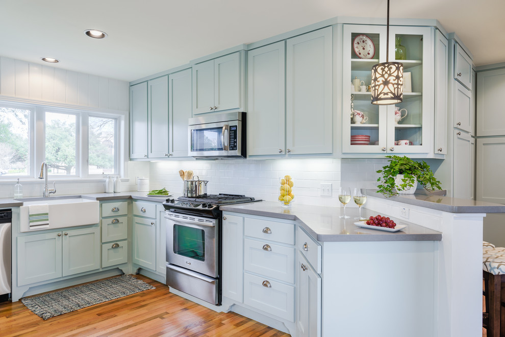 Photo of a midcentury u-shaped eat-in kitchen in Austin with a farmhouse sink, shaker cabinets, blue cabinets, solid surface benchtops, white splashback, subway tile splashback, stainless steel appliances, medium hardwood floors and no island.