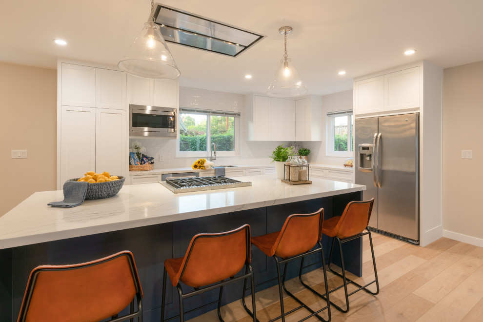 Photo of a mid-sized midcentury l-shaped eat-in kitchen in Santa Barbara with an undermount sink, shaker cabinets, white cabinets, quartz benchtops, white splashback, subway tile splashback, stainless steel appliances, vinyl floors, with island, brown floor and white benchtop.