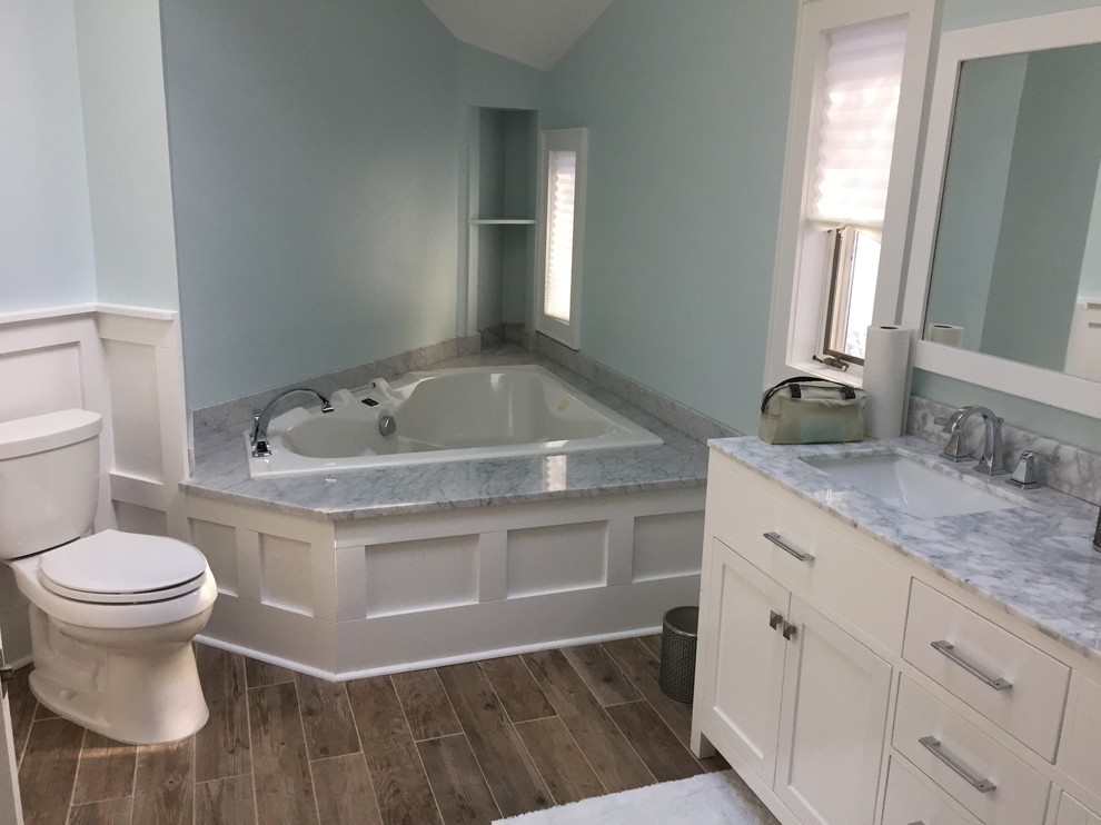 This is an example of a large transitional master bathroom in New York with recessed-panel cabinets, white cabinets, a drop-in tub, an alcove shower, blue walls, vinyl floors, marble benchtops and a hinged shower door.