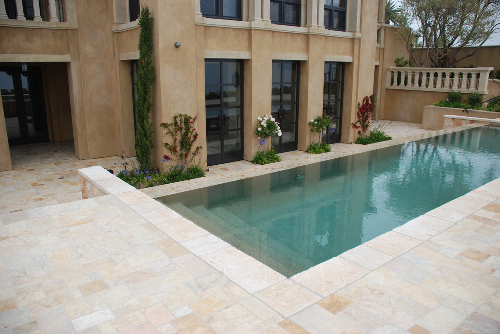 Photo of a mid-sized mediterranean backyard rectangular lap pool in Orange County with a water feature and natural stone pavers.