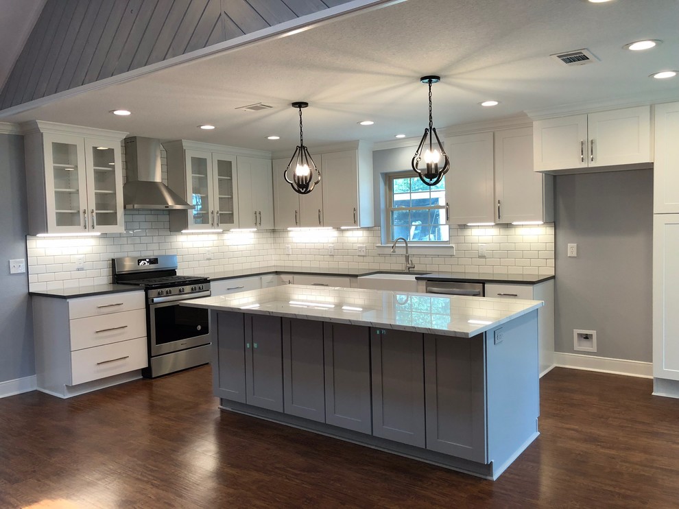 Photo of a mid-sized country l-shaped eat-in kitchen in Austin with a farmhouse sink, shaker cabinets, white cabinets, quartzite benchtops, white splashback, subway tile splashback, stainless steel appliances, vinyl floors, with island, brown floor and white benchtop.