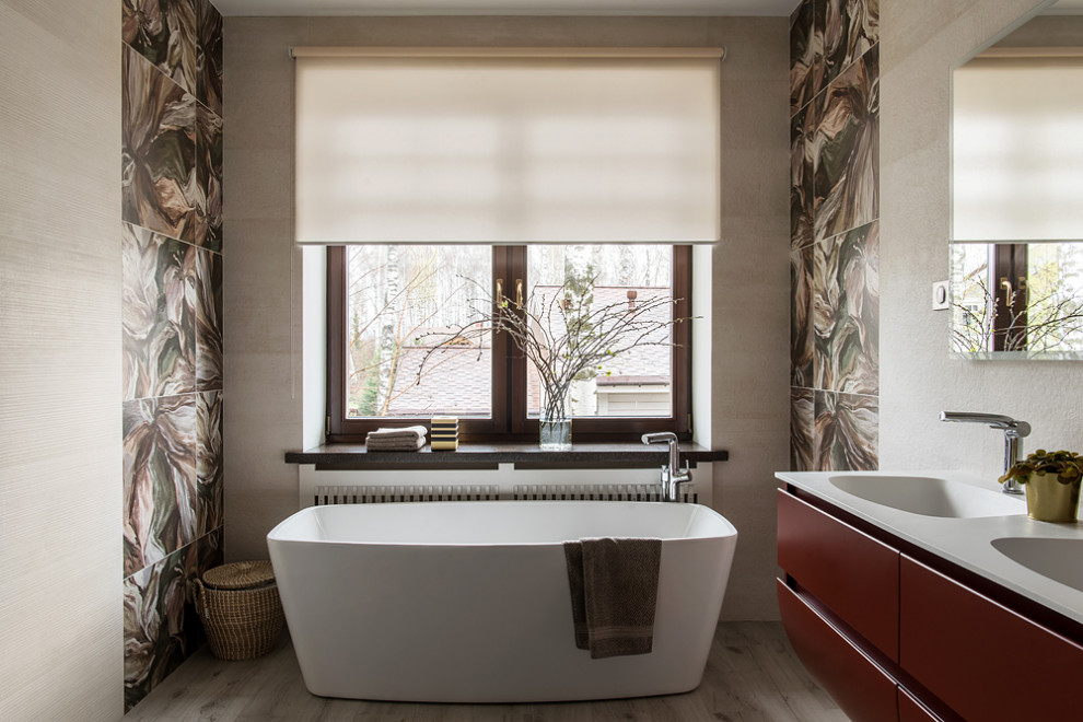 На фото: большая главная ванная комната в современном стиле с плоскими фасадами, красными фасадами, отдельно стоящей ванной, душем в нише, инсталляцией, керамогранитной плиткой, бежевыми стенами, полом из керамогранита, монолитной раковиной, столешницей из искусственного кварца, бежевым полом, душем с распашными дверями, белой столешницей, окном, тумбой под одну раковину и подвесной тумбой с