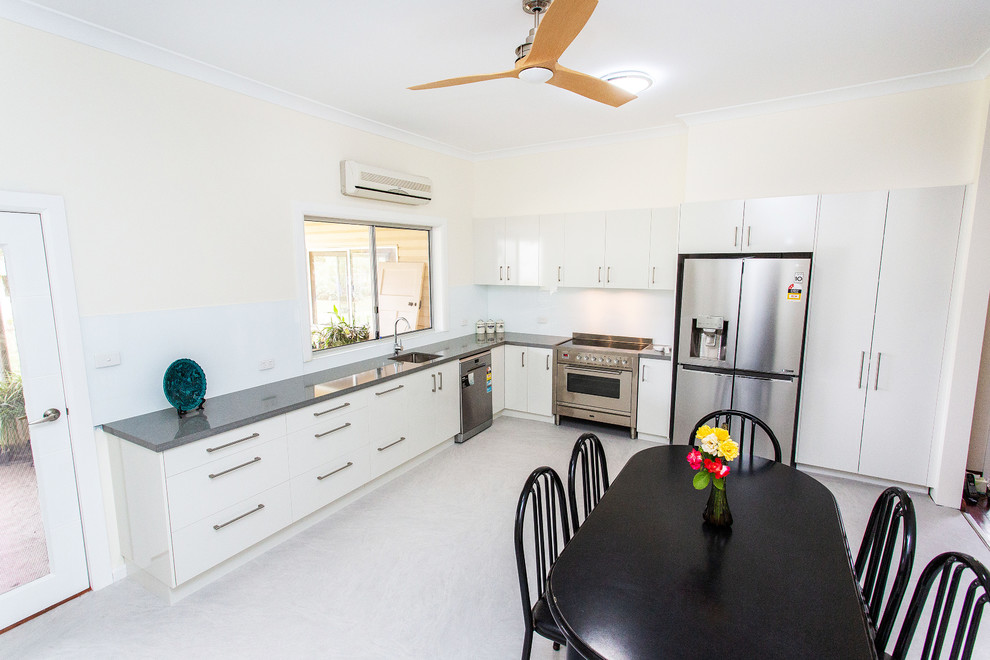 This is an example of a mid-sized contemporary l-shaped eat-in kitchen in Other with an undermount sink, flat-panel cabinets, white cabinets, quartz benchtops, white splashback, glass sheet splashback, stainless steel appliances, linoleum floors, no island, grey floor and grey benchtop.