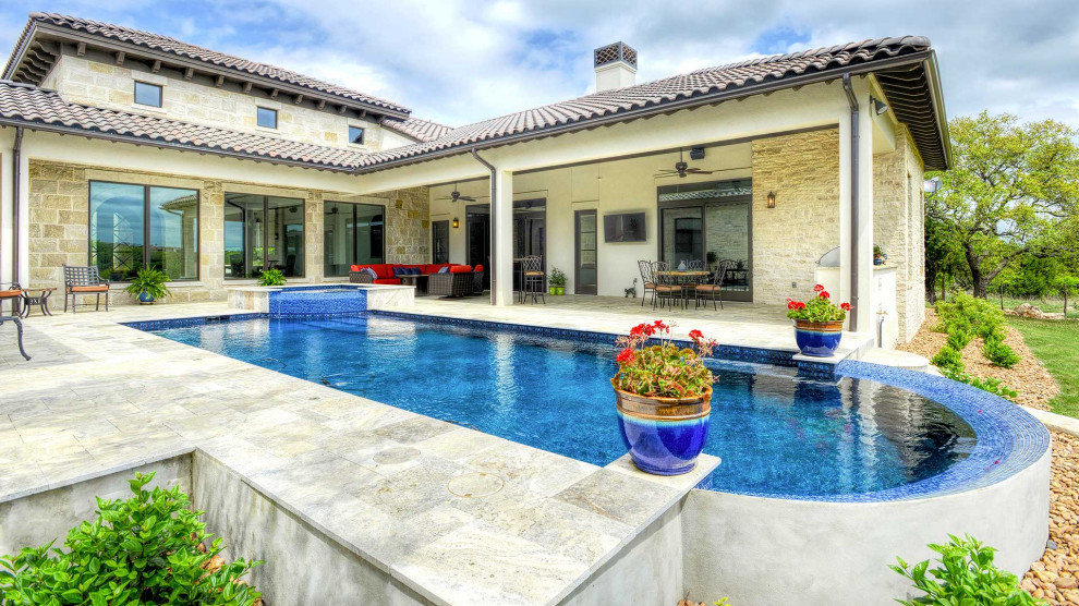 This is an example of a large mediterranean backyard rectangular infinity pool in Austin with natural stone pavers.