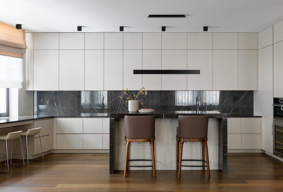 Photo of a contemporary u-shaped open plan kitchen in Moscow with flat-panel cabinets, white cabinets, marble benchtops, black splashback, marble splashback, stainless steel appliances, medium hardwood floors, with island, brown floor and black benchtop.