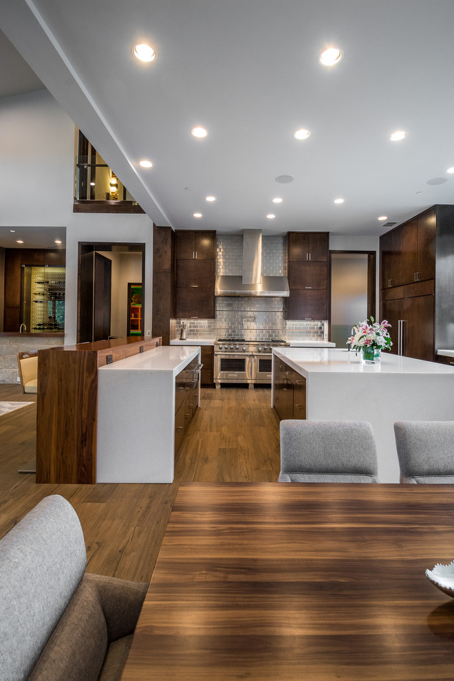 This is an example of an expansive contemporary u-shaped open plan kitchen in Orange County with flat-panel cabinets, brown cabinets, marble benchtops, metallic splashback, metal splashback, stainless steel appliances, porcelain floors, multiple islands and brown floor.