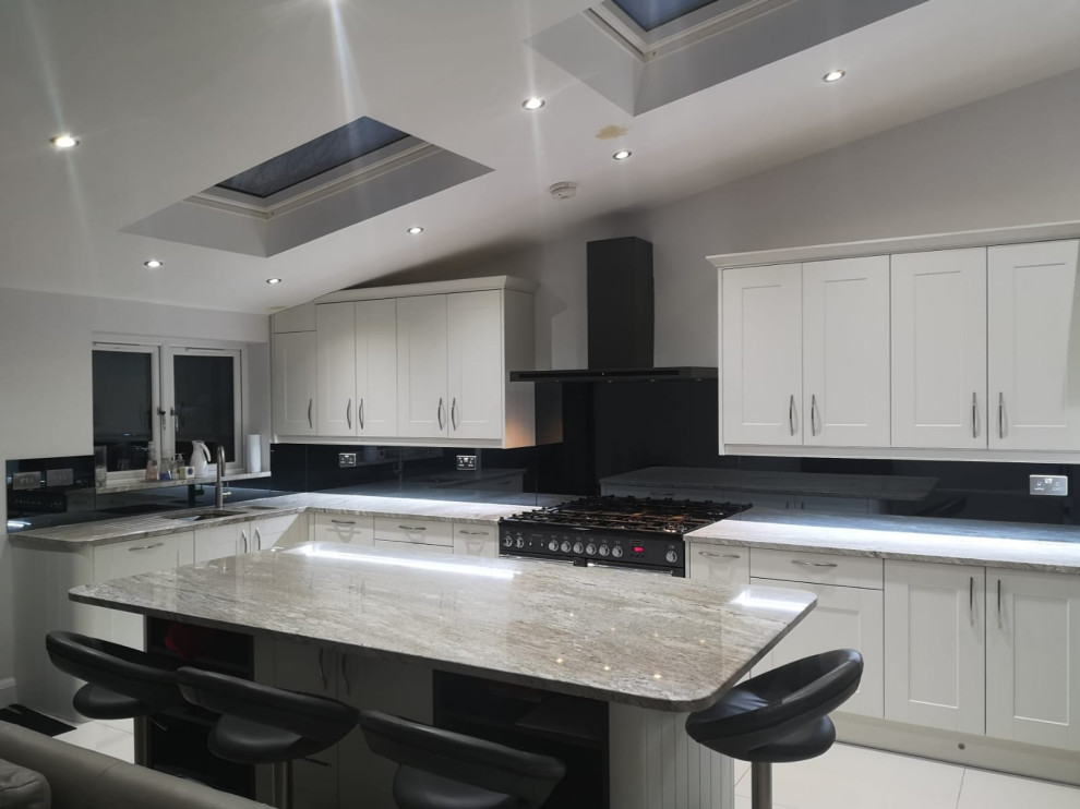 Inspiration for a large country l-shaped eat-in kitchen in London with a double-bowl sink, shaker cabinets, beige cabinets, granite benchtops, grey splashback, mirror splashback, with island and white benchtop.