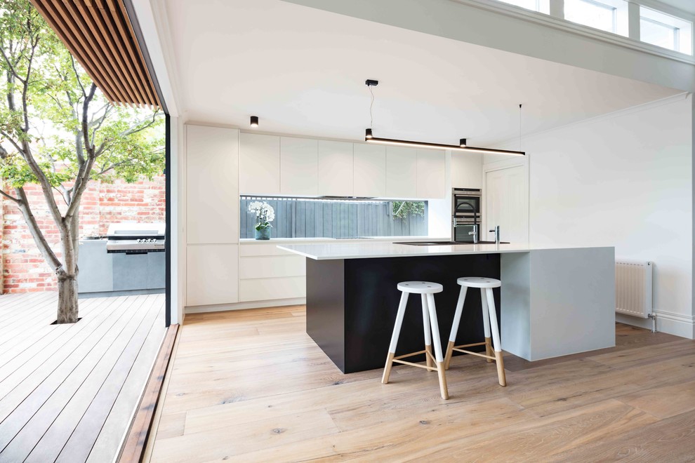 Inspiration for a mid-sized contemporary galley kitchen pantry in Melbourne with a double-bowl sink, white cabinets, marble benchtops, window splashback, stainless steel appliances, light hardwood floors and with island.