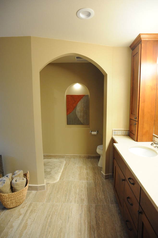 This is an example of a large traditional master bathroom in Milwaukee with an integrated sink, shaker cabinets, medium wood cabinets, solid surface benchtops, a two-piece toilet, multi-coloured tile, porcelain tile, beige walls and porcelain floors.