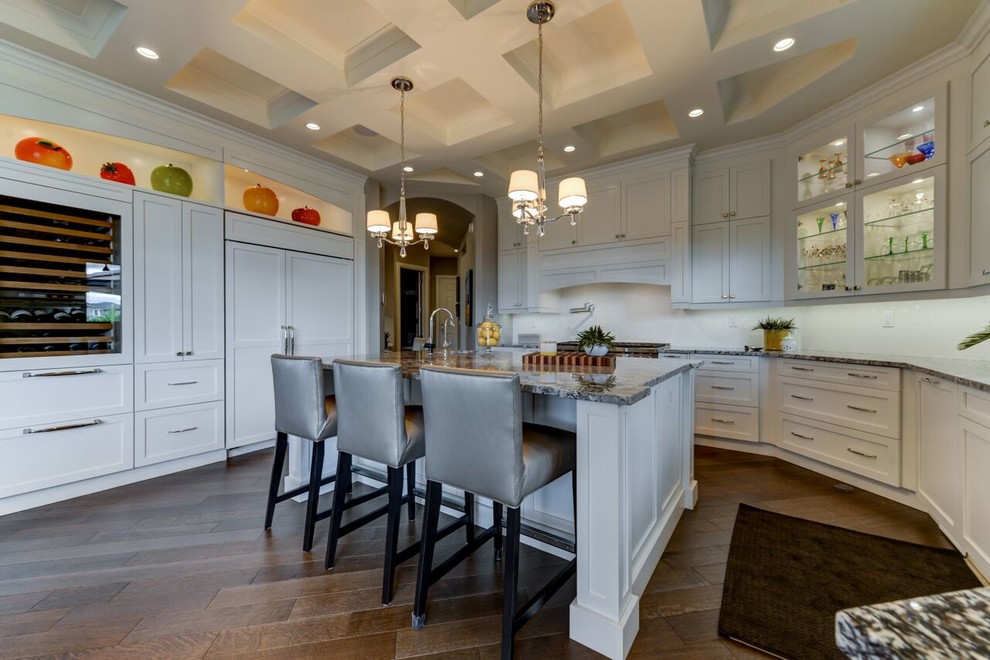 Large transitional u-shaped medium tone wood floor and brown floor kitchen photo in Edmonton with shaker cabinets, white cabinets, granite countertops, white backsplash, an island, paneled appliances, an undermount sink and glass tile backsplash