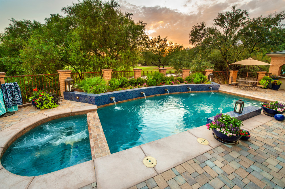 This is an example of a mid-sized contemporary backyard custom-shaped pool in Phoenix with brick pavers and a hot tub.